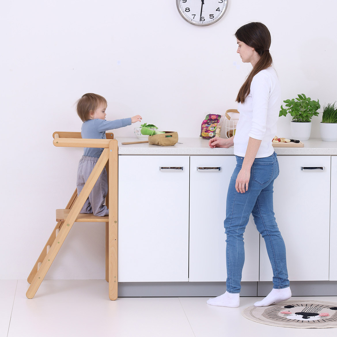 Mother and toddler cooking together in kitchen, child standing on MONTEtower foldable Montessori learning tower by Brubi