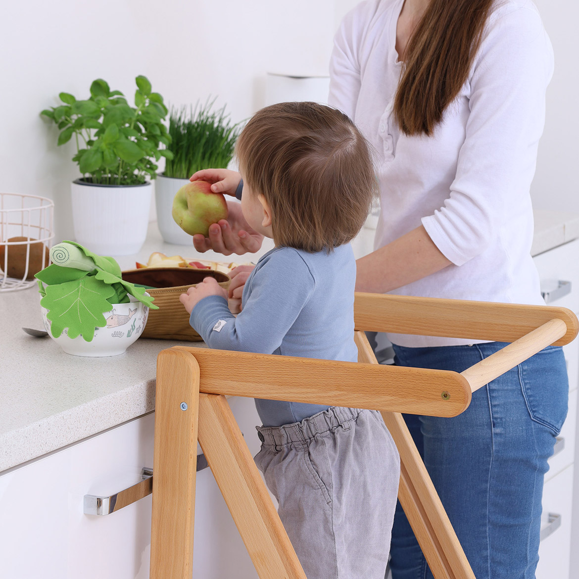 Mother and toddler handling fruit together, child standing on MONTEtower foldable Montessori learning tower by Brubi