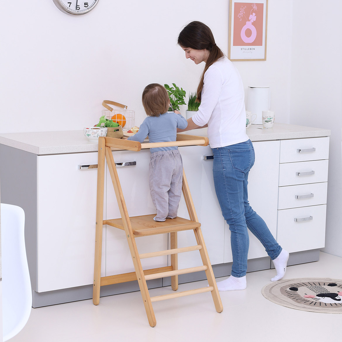 Side view of child and mother at kitchen counter, child standing on MONTEtower foldable Montessori learning tower by Brubi